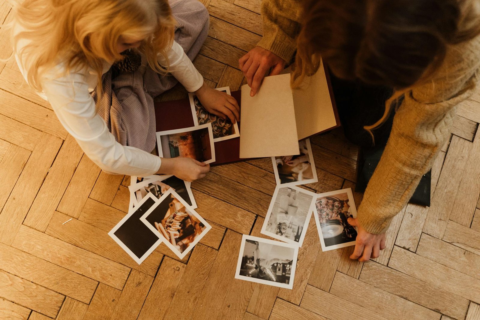 An overhead view of two people sharing and organizing photographs on the wooden floor.
